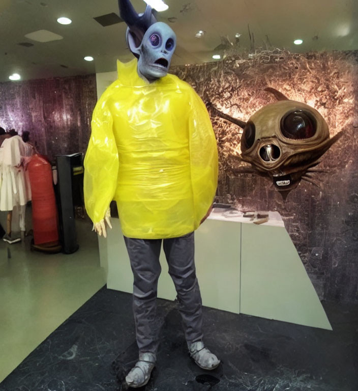 Person in Alien Costume with Yellow Inflatable Suit Next to Large-Eyed Alien Head