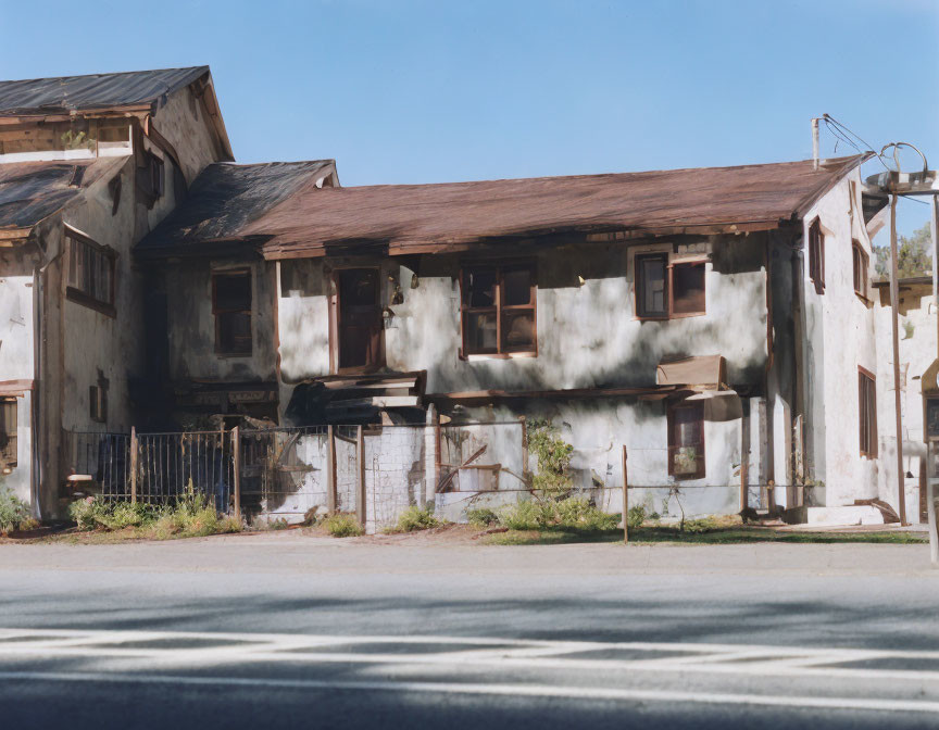 Abandoned two-story buildings with boarded-up windows under clear blue sky