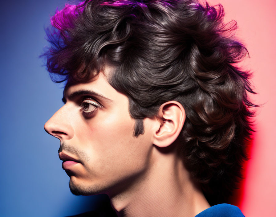 Young man with voluminous curly hair on colorful blue and red background