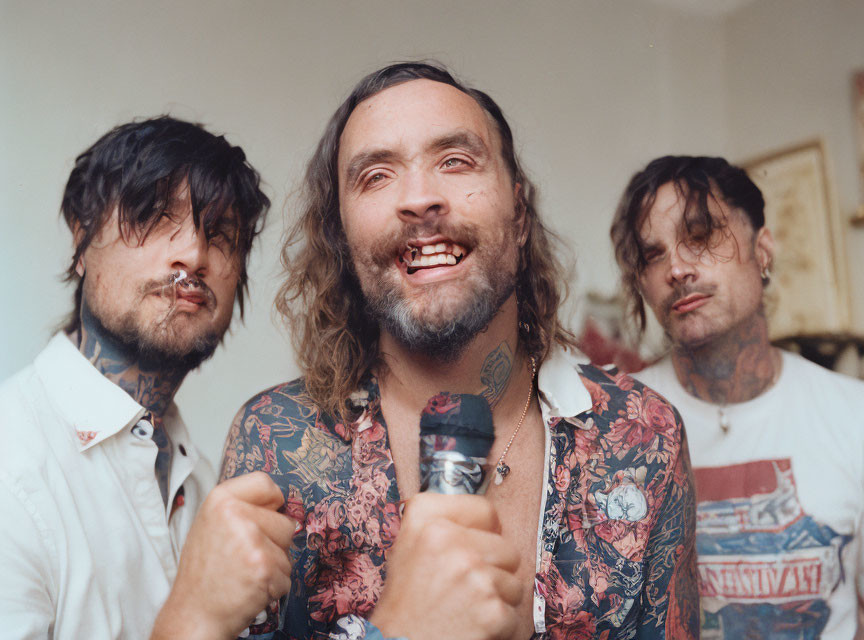 Three Men with Tattoos and Piercings Posing Intensely in White Room