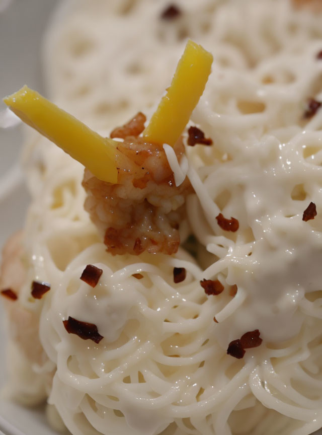 Creamy pasta dish with grated cheese, bacon bits, and yellow bell pepper slices