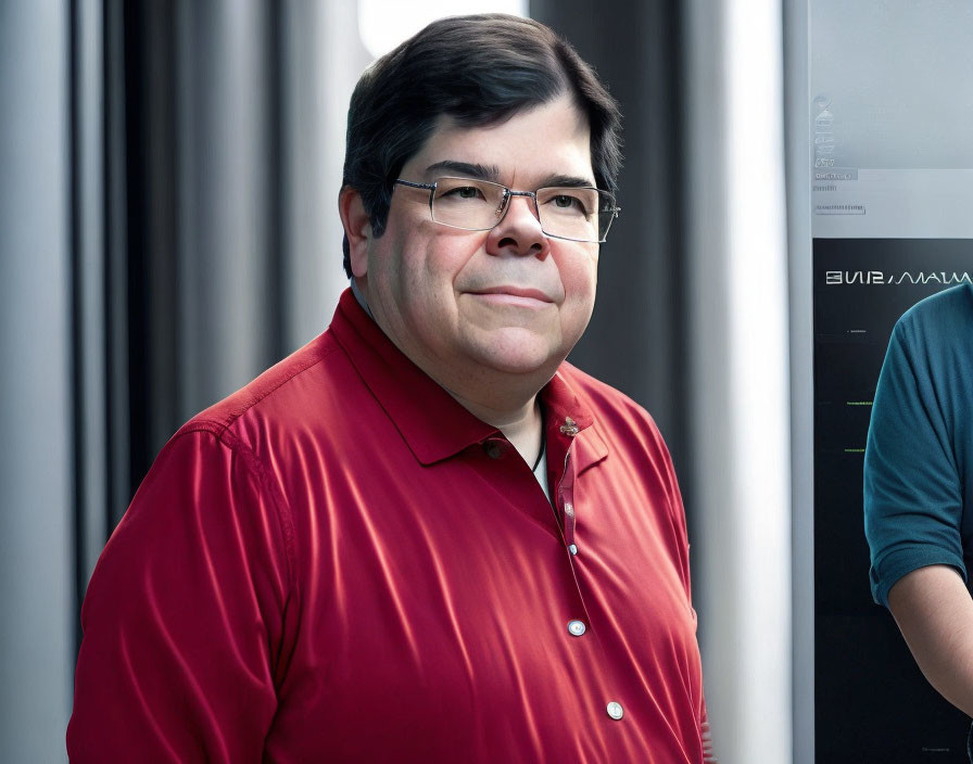 Man in glasses confidently stands in red shirt indoors