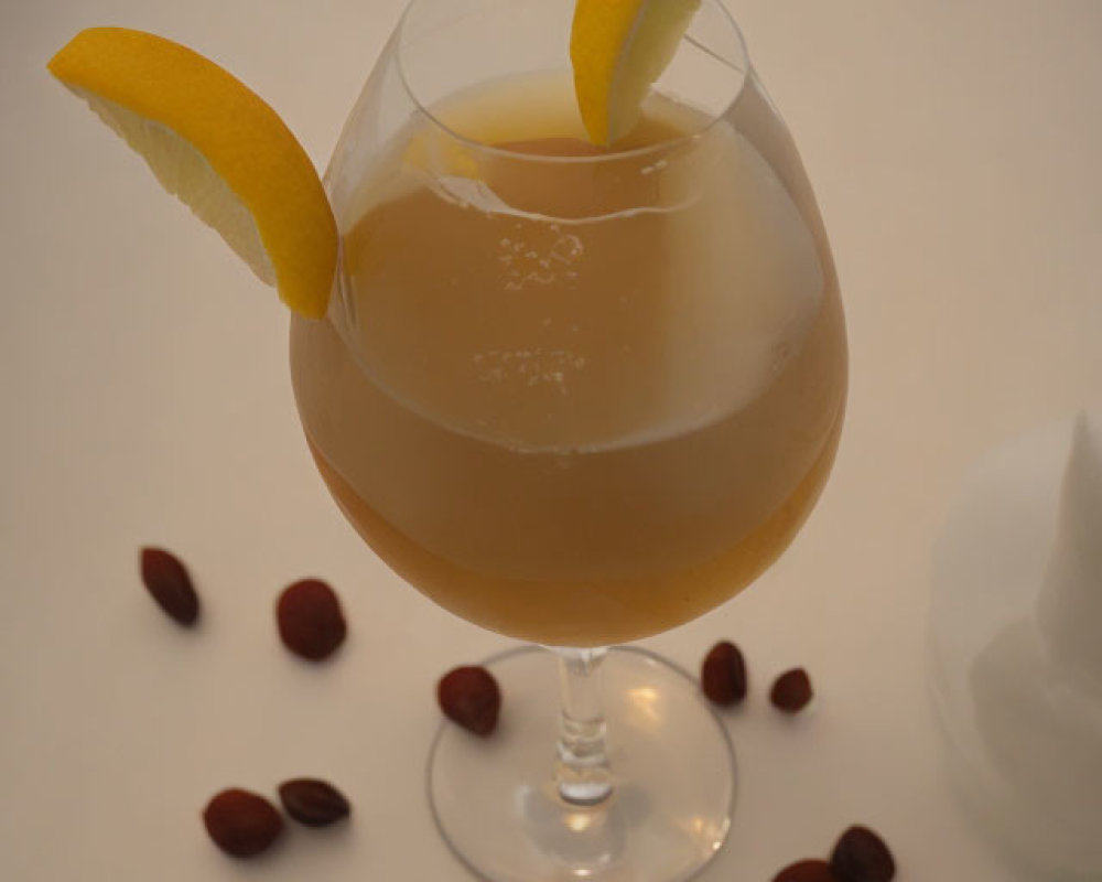 Golden beverage in stemmed glass with lemon slices and almonds on white surface