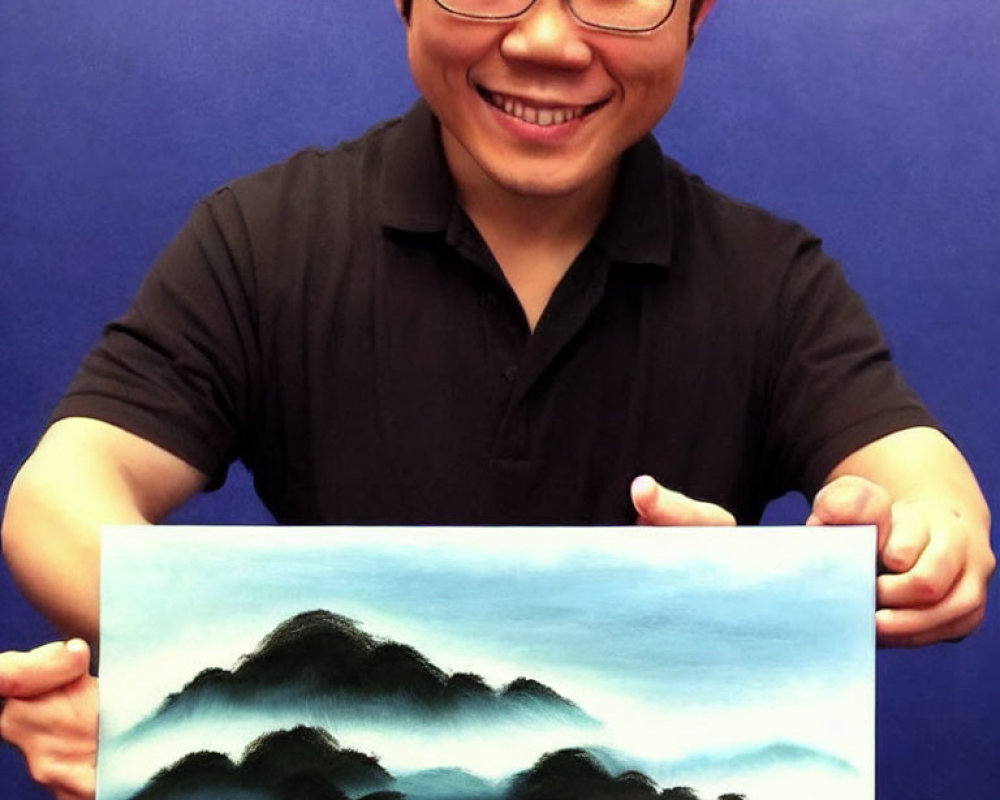 Smiling man with glasses holding landscape painting of misty mountains