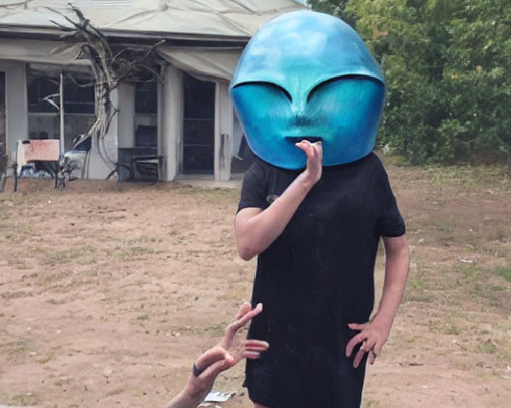 Person wearing oversized alien head mask in front of dilapidated building with reaching hand