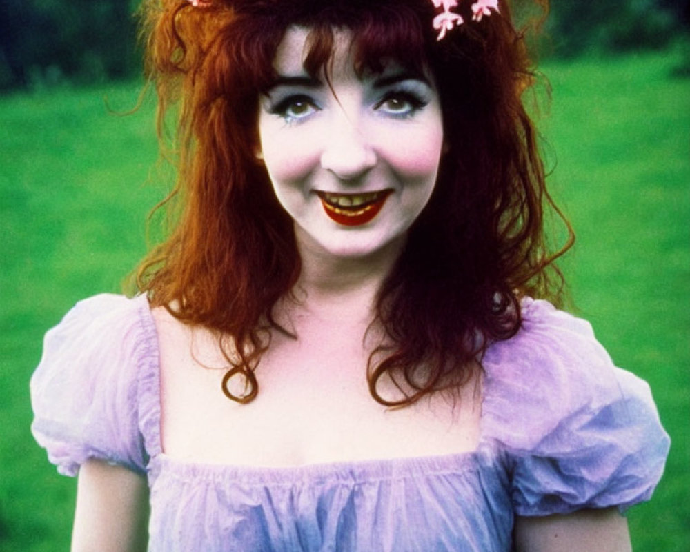 Red-haired woman in pink floral wreath and purple dress smiling outdoors.