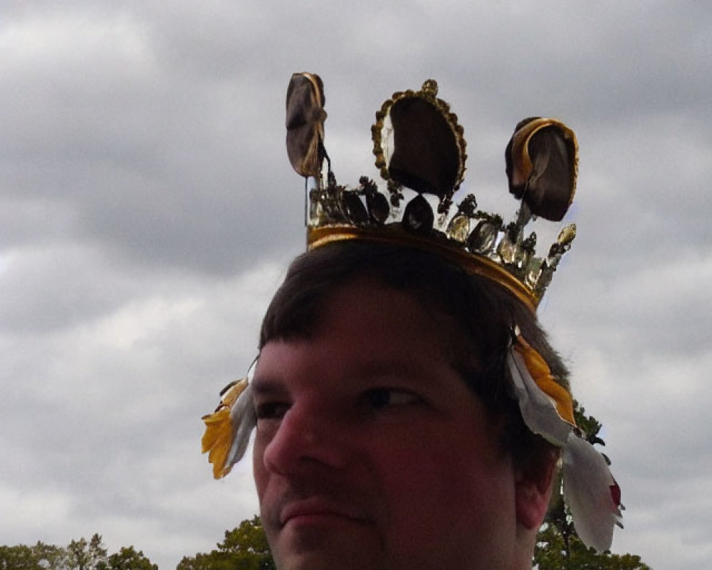 Feathered crown on person with bird figurines against cloudy sky