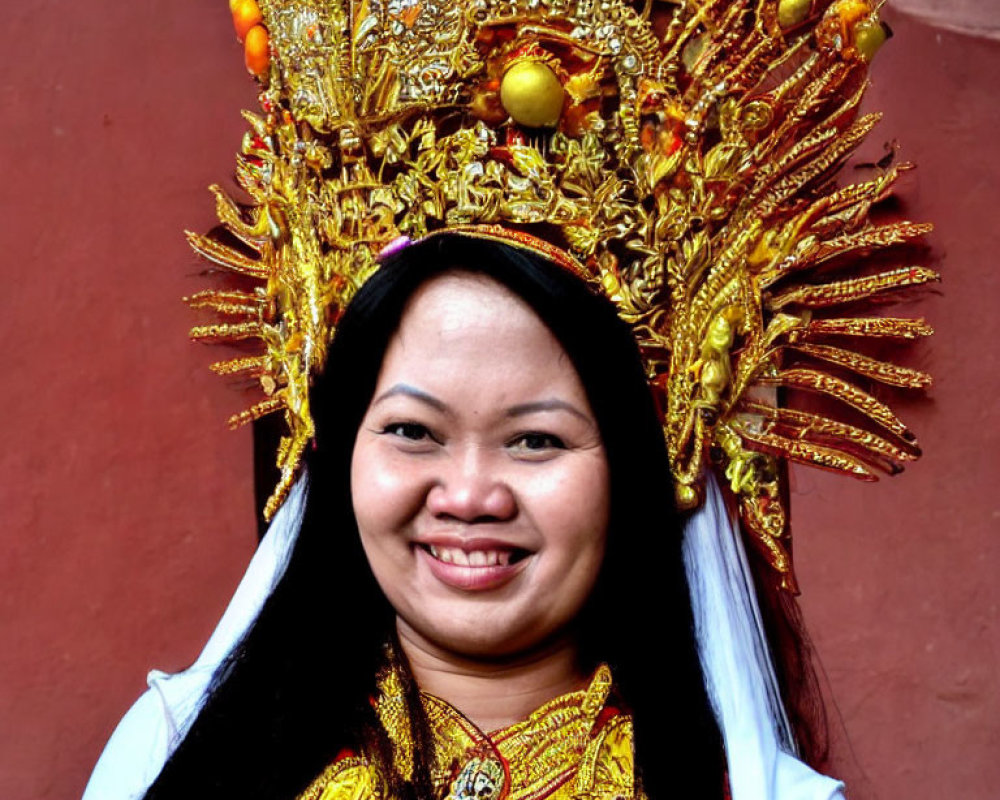 Traditional headdress adorned with gold and fruit on smiling woman against reddish-brown backdrop