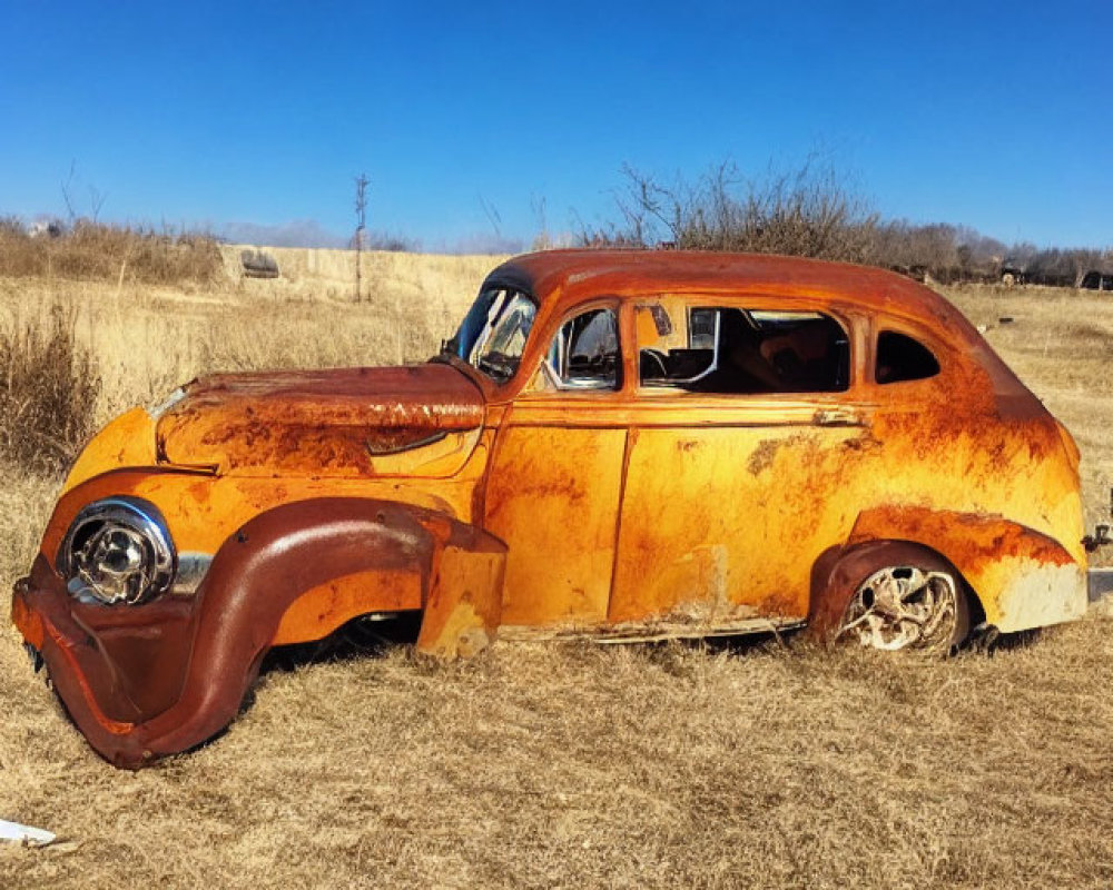 Rusted abandoned car in dry grass field under blue sky