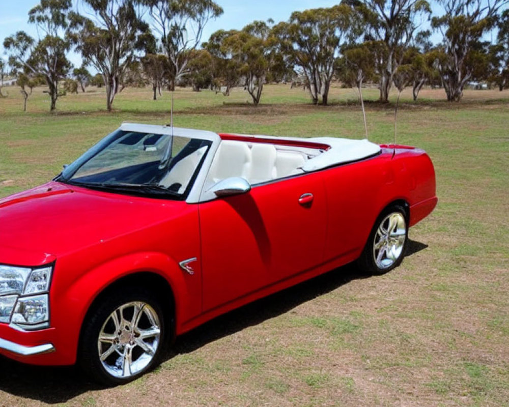 Red Convertible Car Parked with Top Down on Grass Field and Trees Against Blue Sky