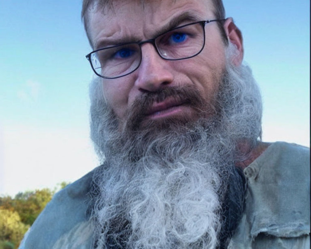 Intense man with wavy beard and glasses against blurred nature backdrop