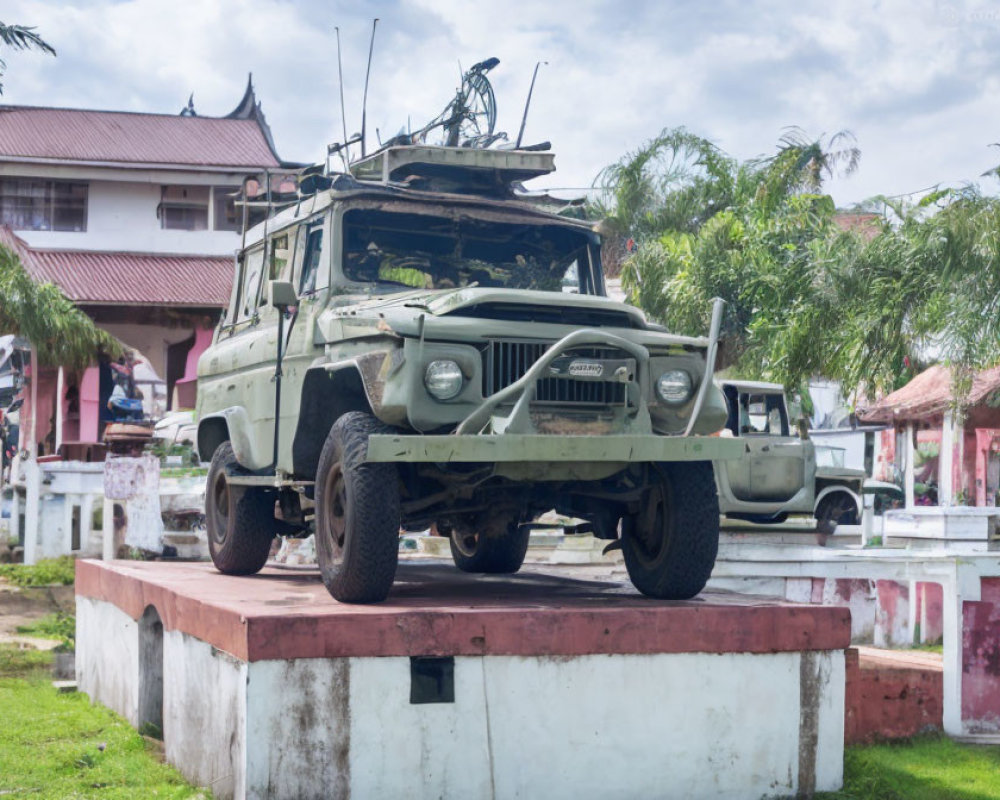 Military jeep with antenna and mounted gun on white pedestal, building in background