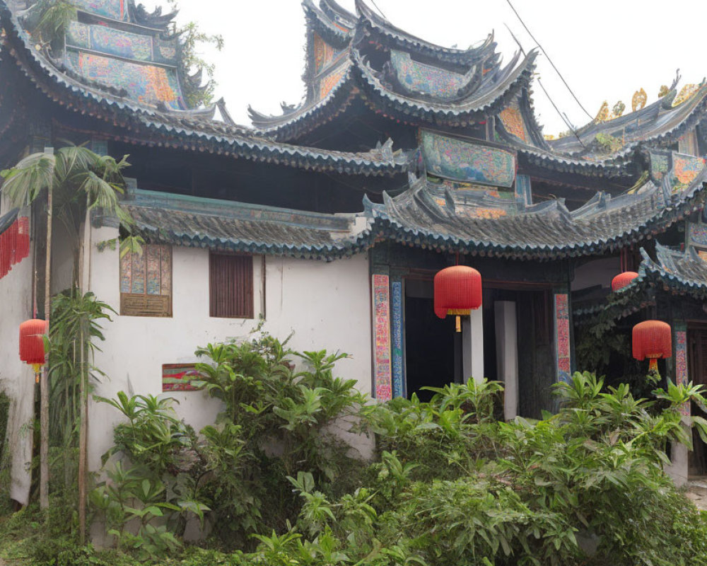 Traditional Chinese architecture with upturned roofs and red lanterns amidst green shrubbery