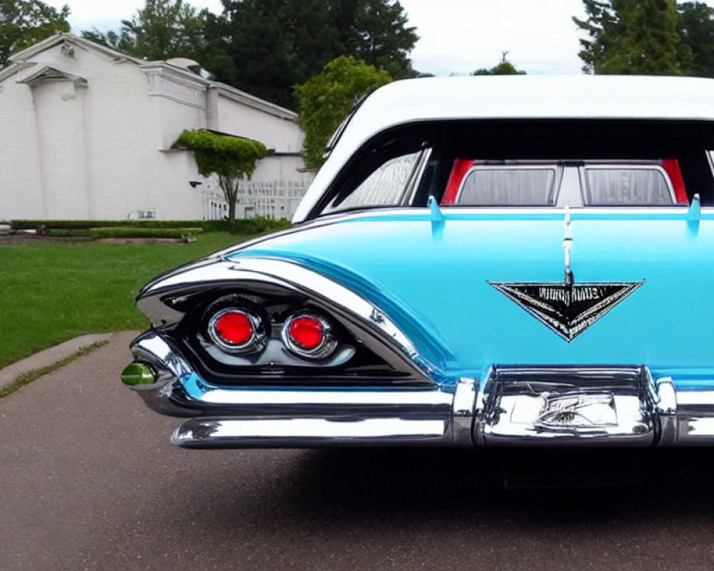 Vintage blue car with tail fins parked in front of white building with greenery