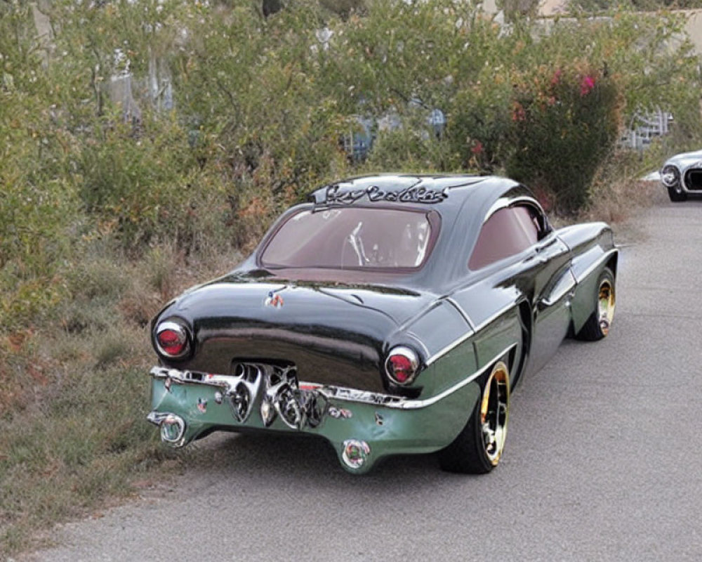 Vintage green car with flame decals and white wall tires parked by roadside shrubs.