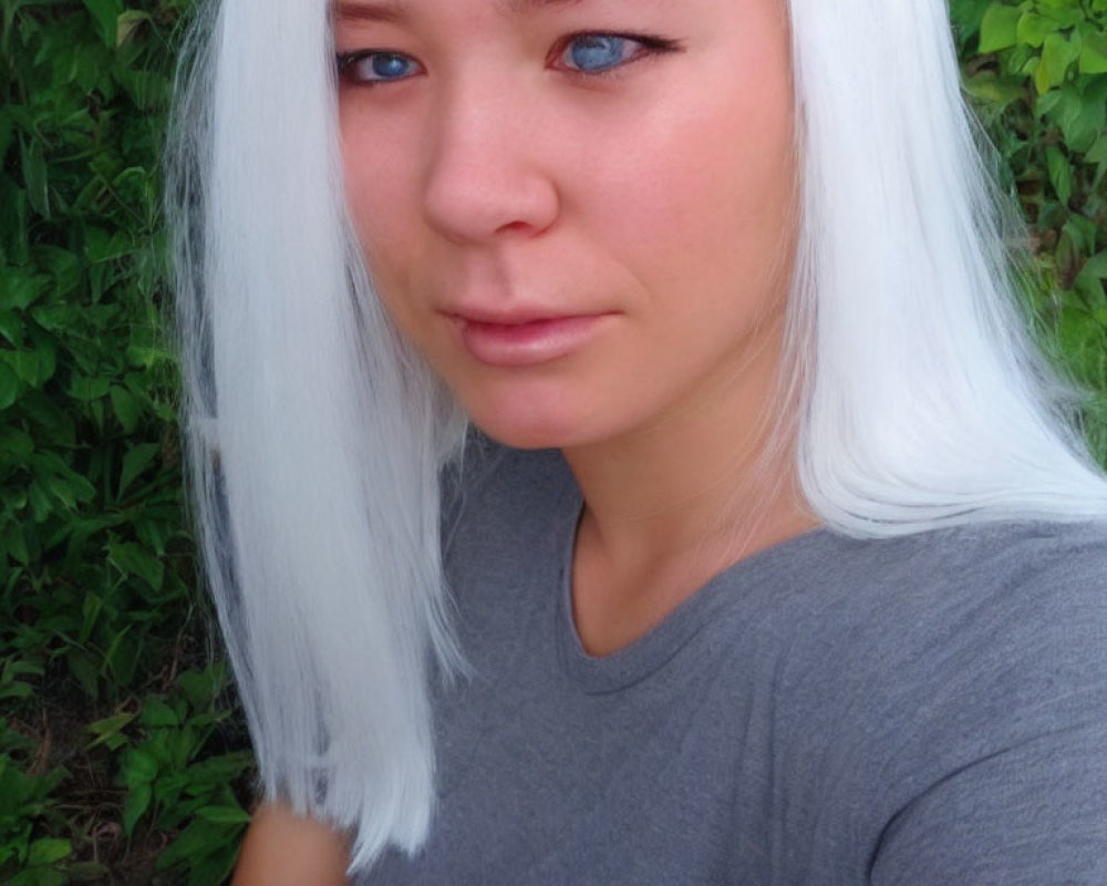 Portrait of a person with bright blue eyes and white hair on green leafy backdrop