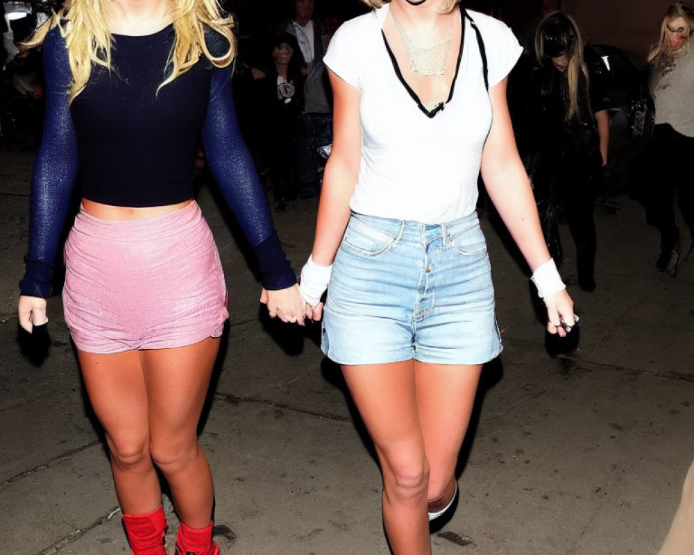 Two women in different outfits walking hand in hand with red lipstick.