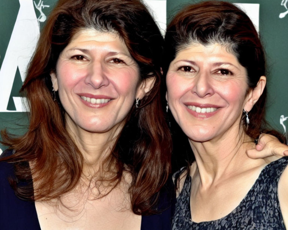 Twin women smiling in dark tops with curly hair on green background