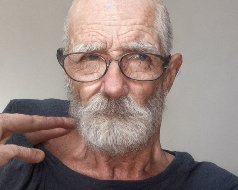 Gray-bearded elderly man in glasses and black T-shirt gesturing by face