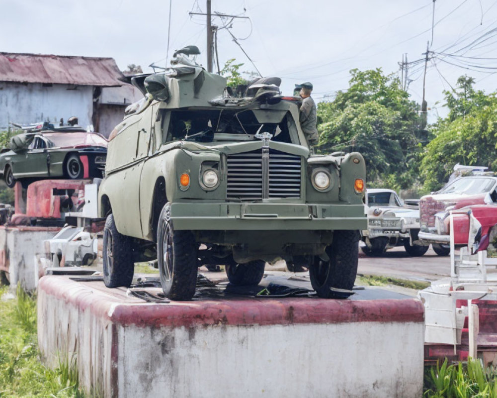 Military personnel on armored vehicle in fenced area with military and civilian vehicles.