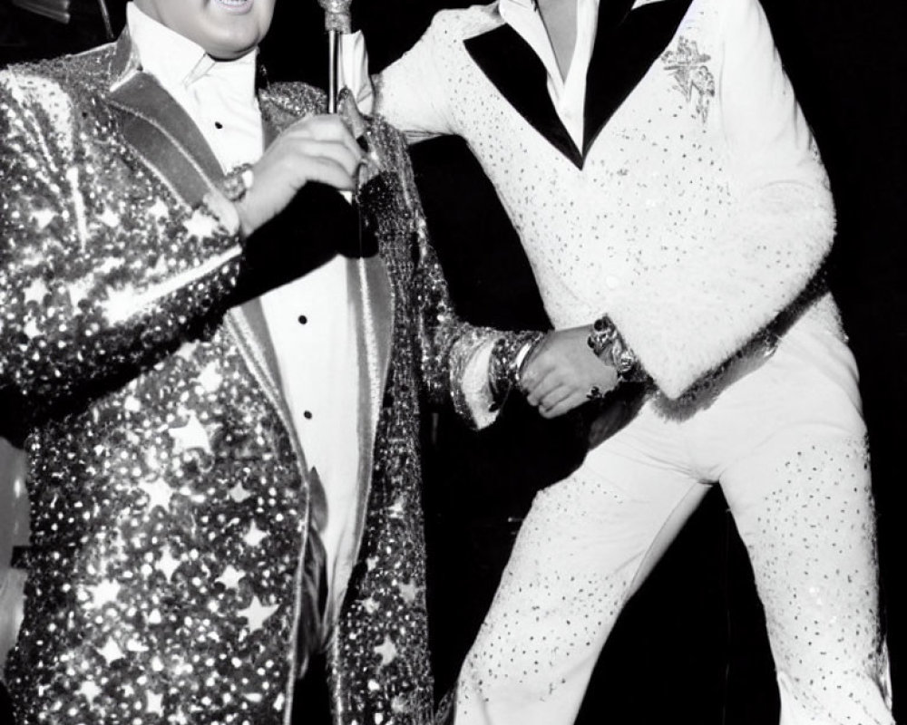 Two Elvis Impersonators in Sparkling Outfits Holding Microphones in Black and White Photo