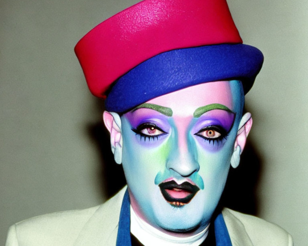 Colorful makeup look with pink top hat, blue eyeshadow, bold eyebrows, and purple lipstick