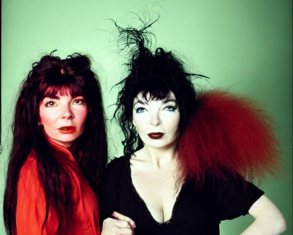 Two women with dramatic makeup and wild hairstyles on green background