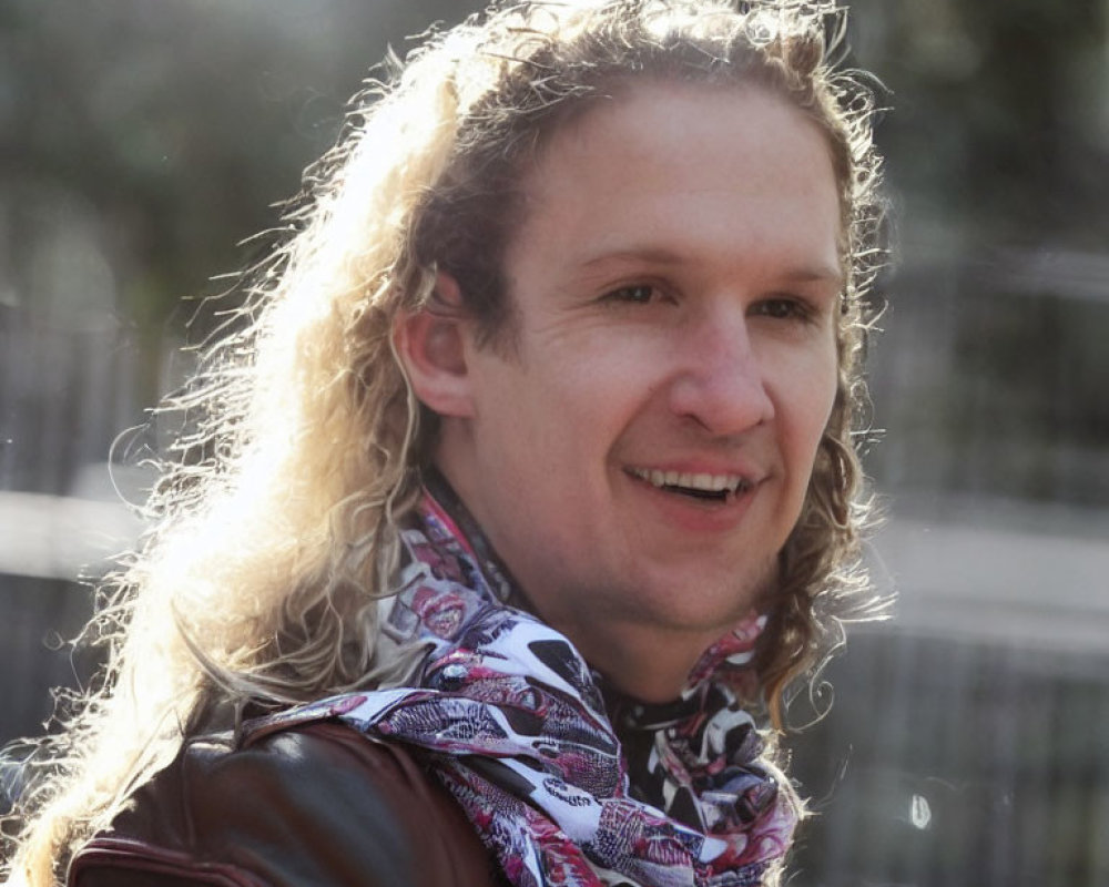 Blond man in leather jacket and scarf smiling outdoors