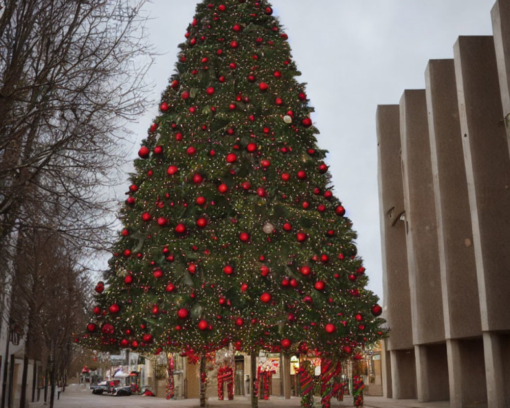 City sidewalk Christmas tree with red ornaments and lights near modern buildings under cloudy sky