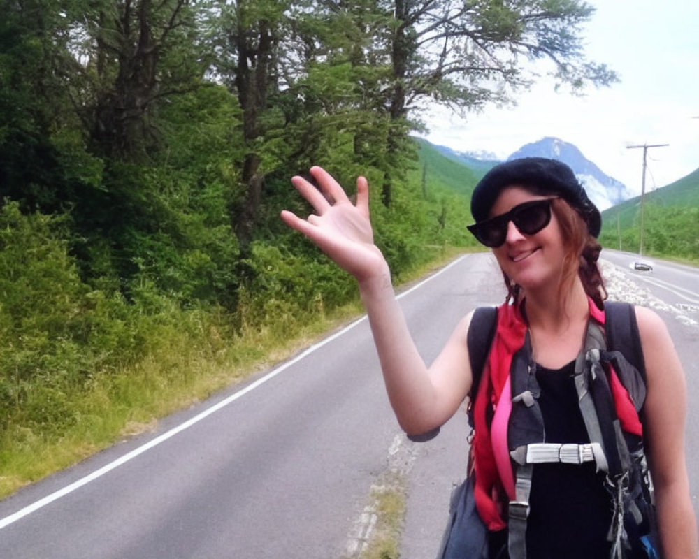 Smiling woman with backpack, hat, and sunglasses waving on roadside