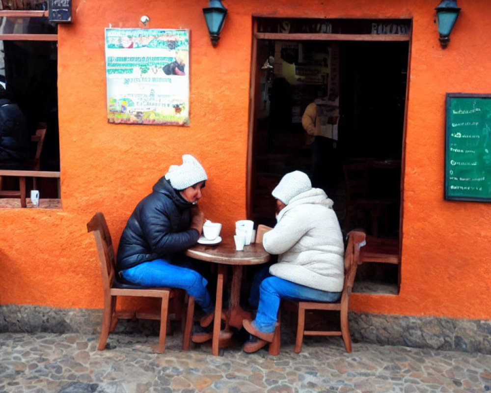 Two individuals at outdoor cafe table on cobblestone sidewalk