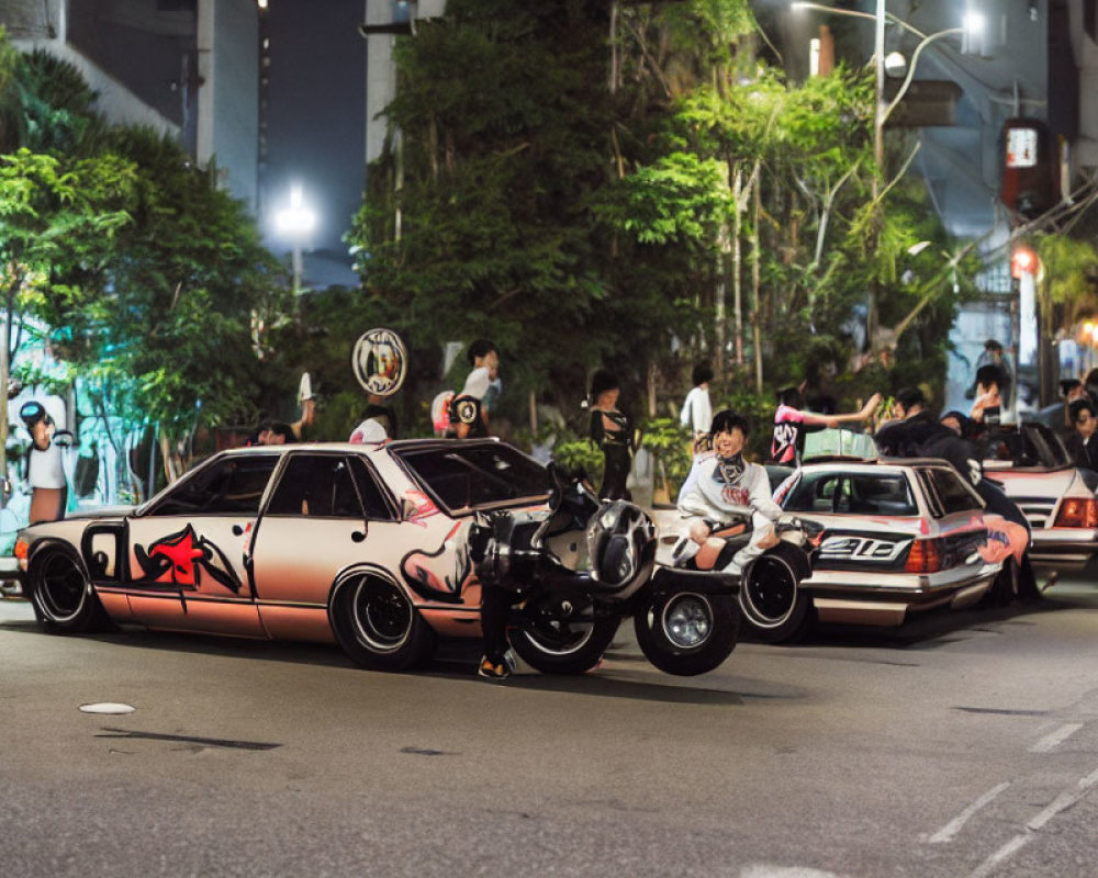 Group of people admiring modified pink and black cars on city street at night