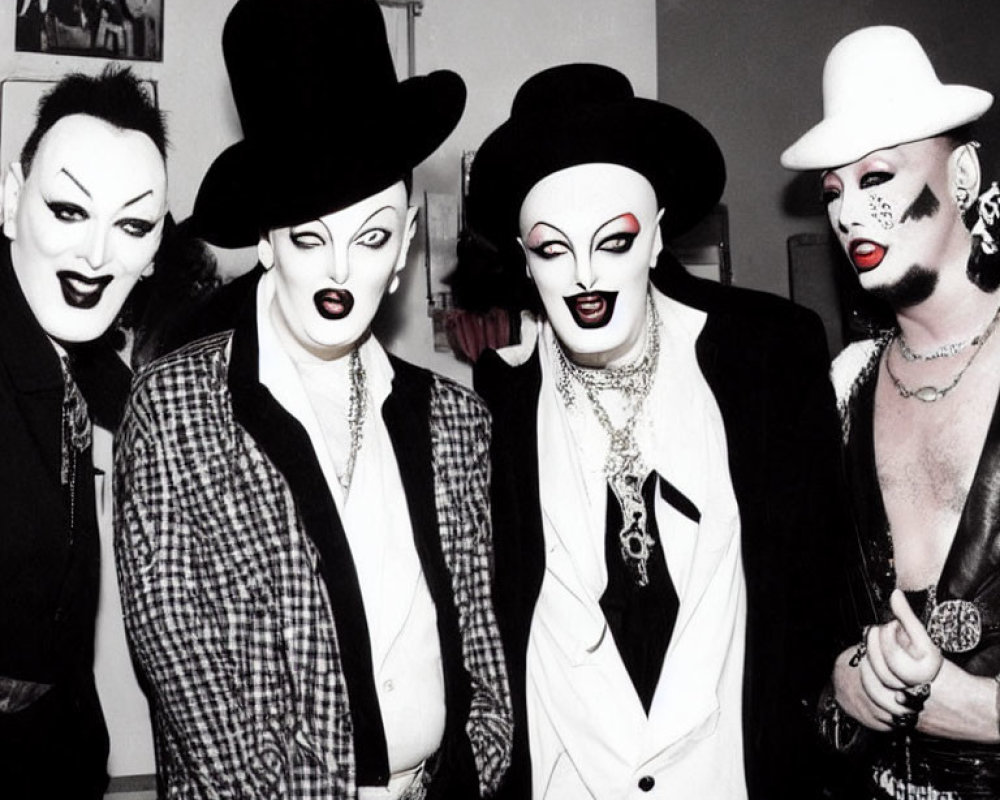 Four individuals in dramatic makeup and costumes with exaggerated facial expressions, wearing black hats and white suit elements.