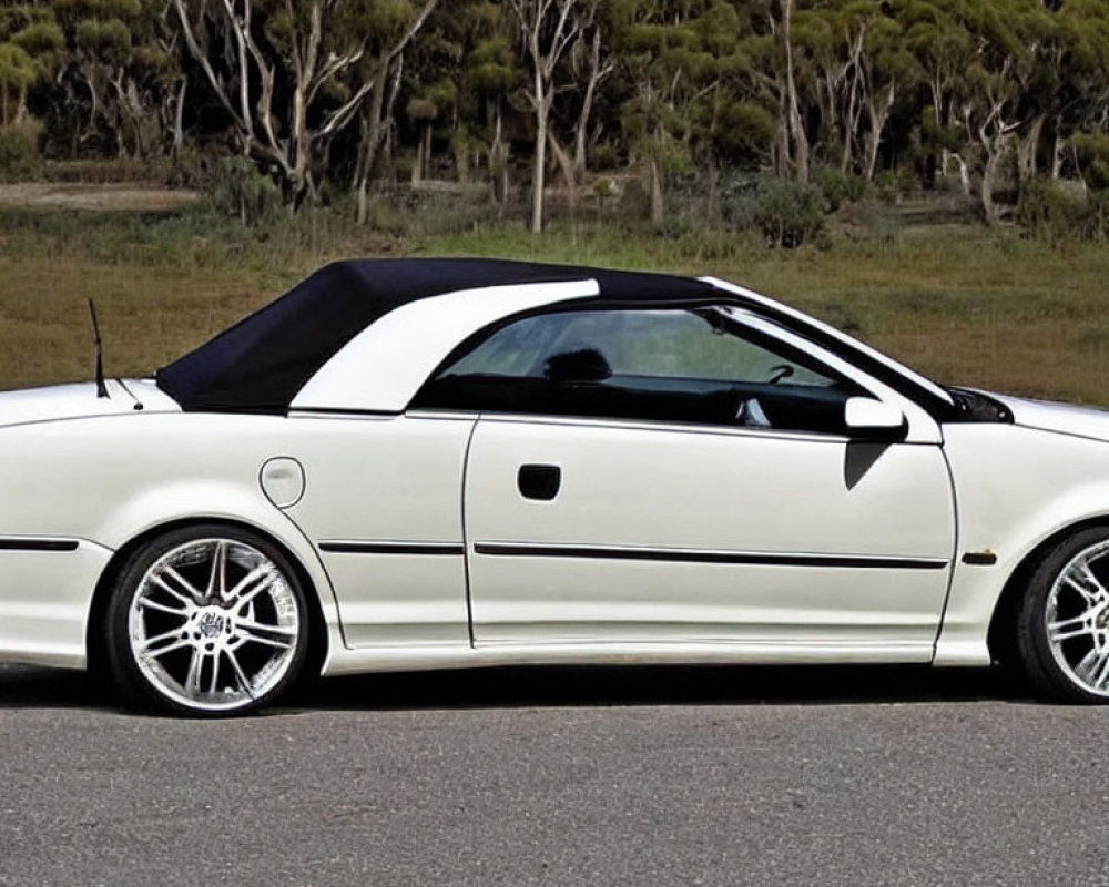 White Convertible Car with Black Soft Top and Aftermarket Wheels Parked by Roadside