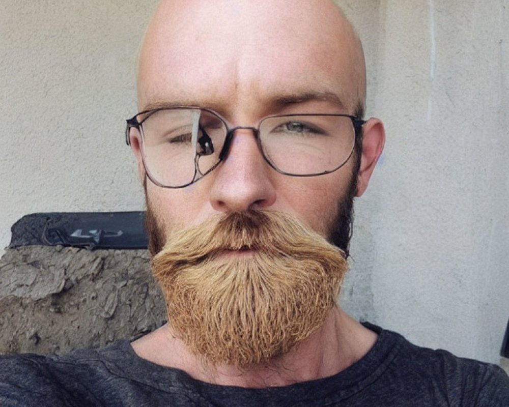 Bald man with twirled mustache in glasses and grey T-shirt