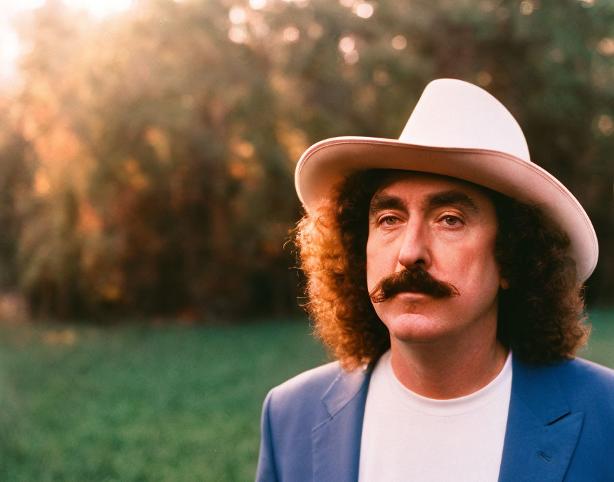 Man with Prominent Mustache in White Hat and Blue Jacket on Blurred Green Background