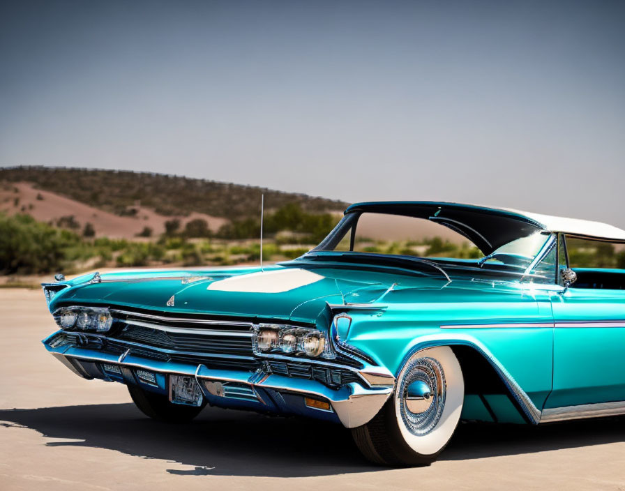 Vintage turquoise and white car with chrome detailing on concrete, set against hilly landscape