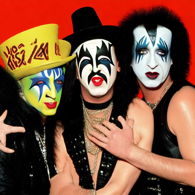 Three individuals in KISS-inspired makeup and costumes on red backdrop