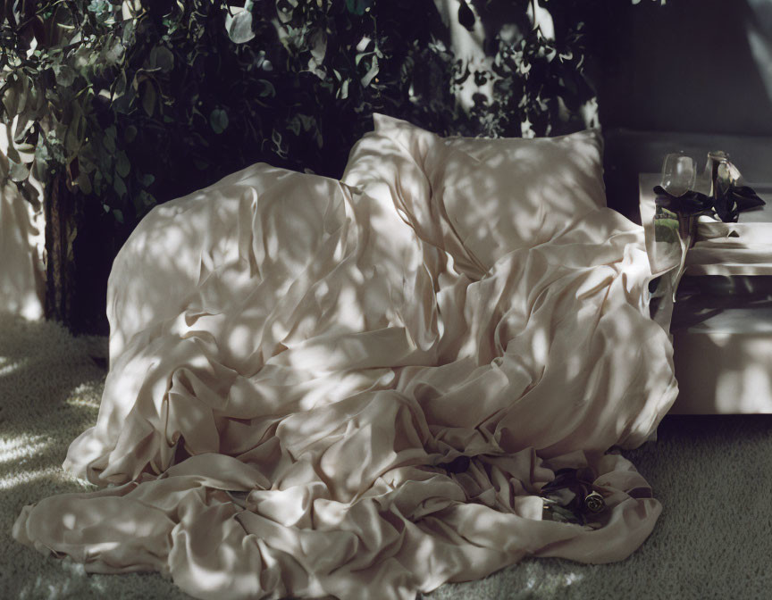 Satin fabric draped among potted plants and perfume bottles on a table