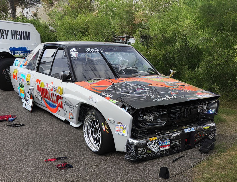 Modified black racing car with vibrant decals and exposed engine parked near trailer