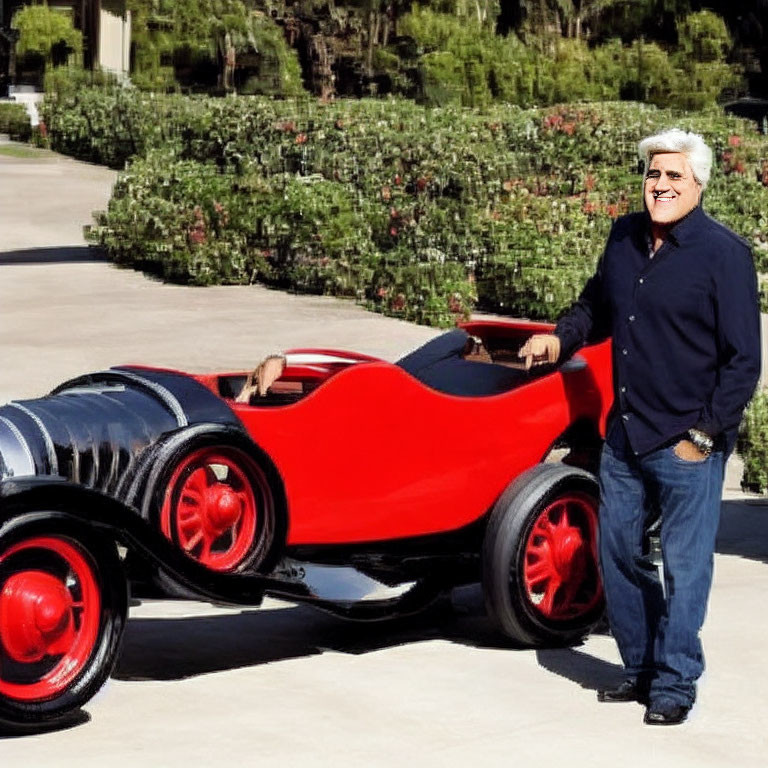 Man smiling beside vintage red and black car on sunny day