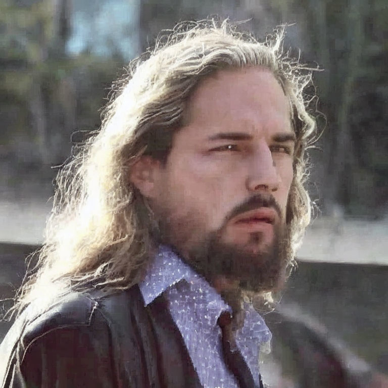 Long-haired man in collared shirt looks pensive.