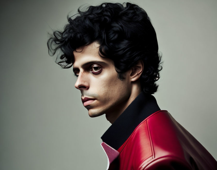 Curly-Haired Man in Red Leather Jacket and Pink Shirt on Grey Background