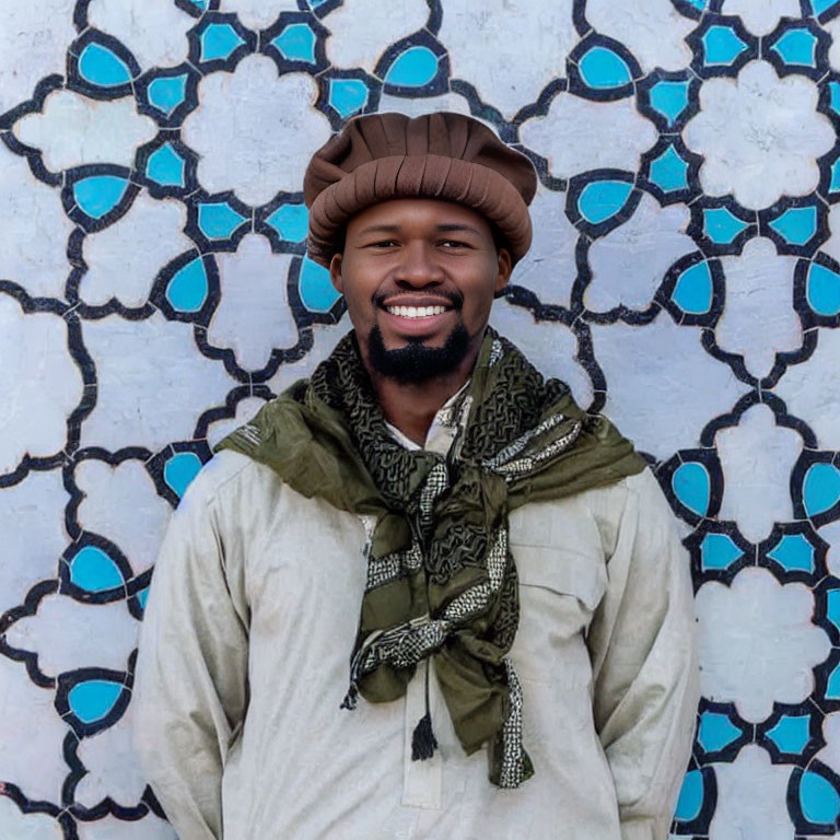 Smiling man with beard in brown hat and scarf against blue patterned wall