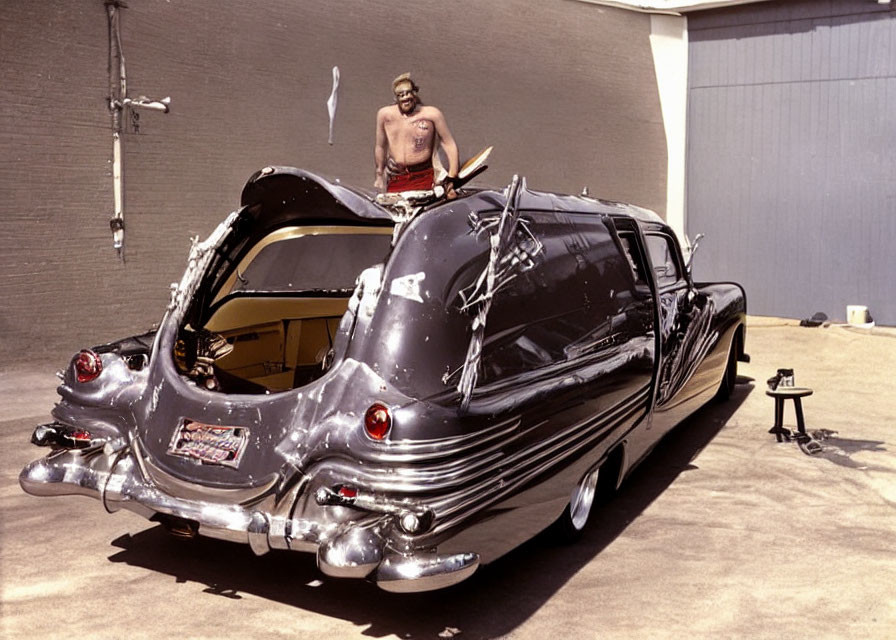 Bare-chested man with surfboard on sleek black vehicle