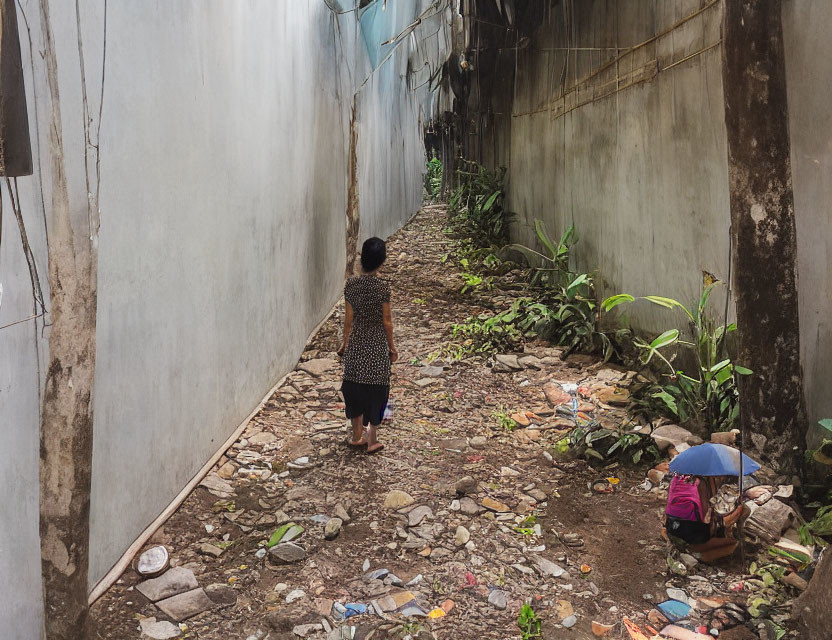 Urban alleyway scene with walking person and umbrella-sitting individual