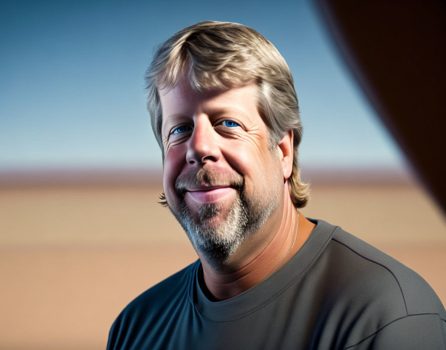 Blonde man with beard smiles against arid backdrop