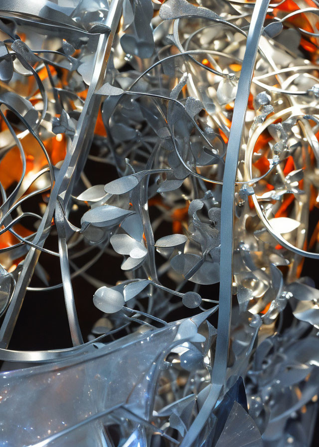 Reflective silver metallic sculpture with entwined leaves and orange highlights.