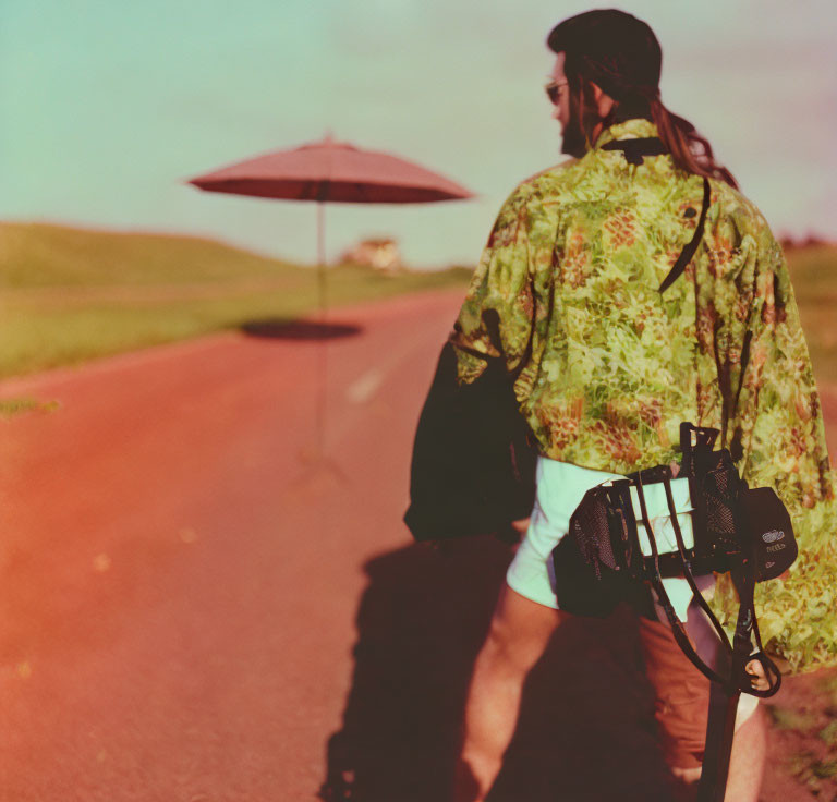 Photographer in green patterned outfit walking with red umbrella on road