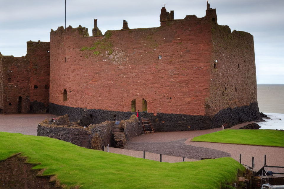 Red-Stone Castle by the Sea with Green Grass and Cloudy Sky